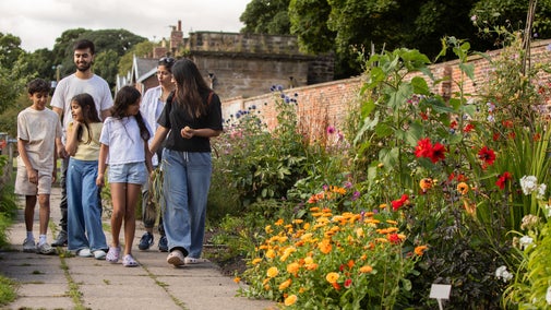 A family walks along a path in a kitchen garden with a border of bright summer flowers to their right